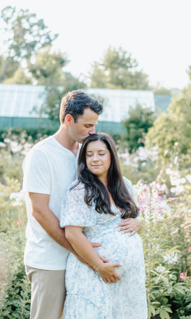 garden maternity session, dad holding moms belly kissing top of her head 